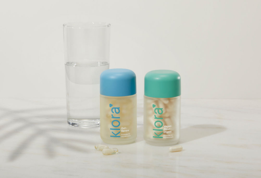 Klora Gut-Renew and Bloat-Digest Health supplement bottles on counter with glass of water and leaf shadow